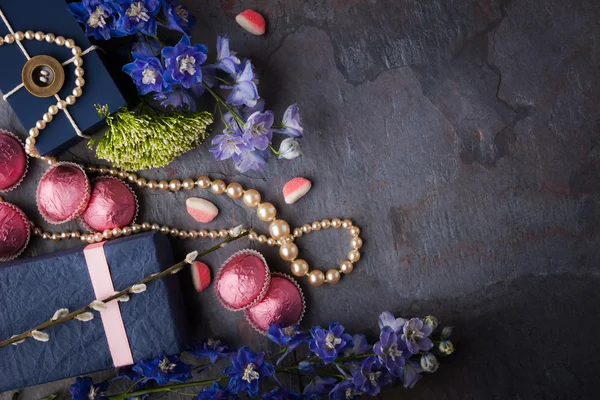 Presente de primavera com doces, colar de pérolas e flores em um sto azul — Fotografia de Stock