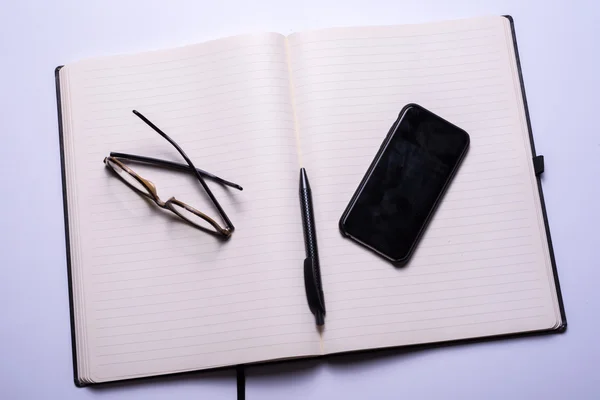 Open Notebook with pen, glasses and smartphone — Stock Photo, Image