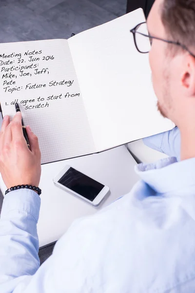 Young man is taking meeting notes in open notebook — Stock Photo, Image
