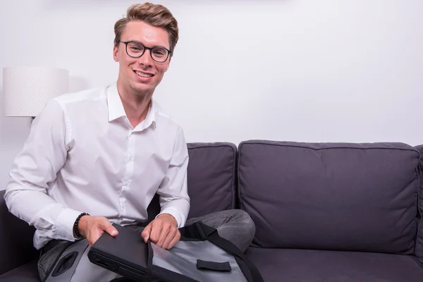 Young smiling business man packing his bag on couch — Stock Photo, Image