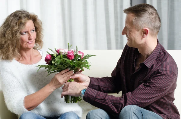 Man is giving a bouquet of flowers to woman - she is in doubt