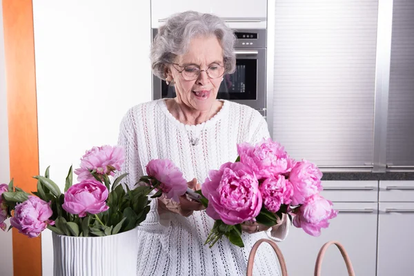 Active female pensioner is preparing flowers for the vase — Stock Photo, Image