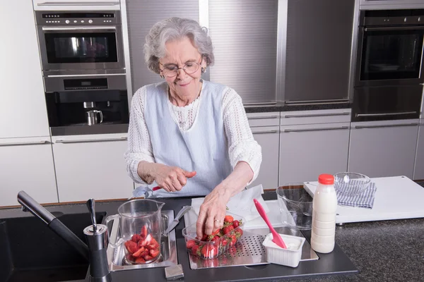 Active female pensioner is preparing and eating strawberries in — Stock Photo, Image