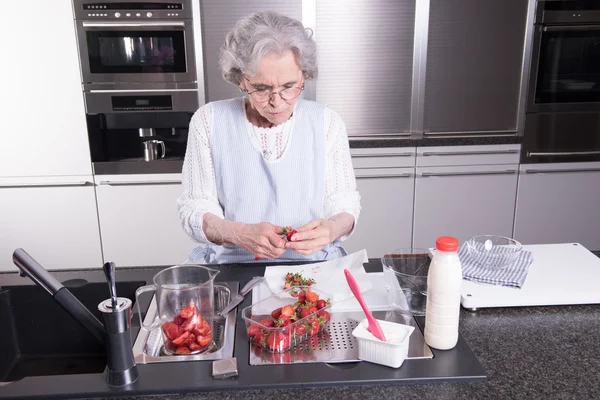 Active female pensioner is preparing strawberries in the kitchen — Stock Photo, Image