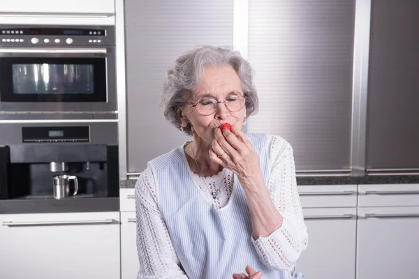 Pensionista femenina activa está degustando fresas en la cocina —  Fotos de Stock