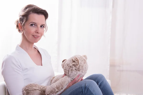 Kvinna sitter i fåtölj med teddy — Stockfoto