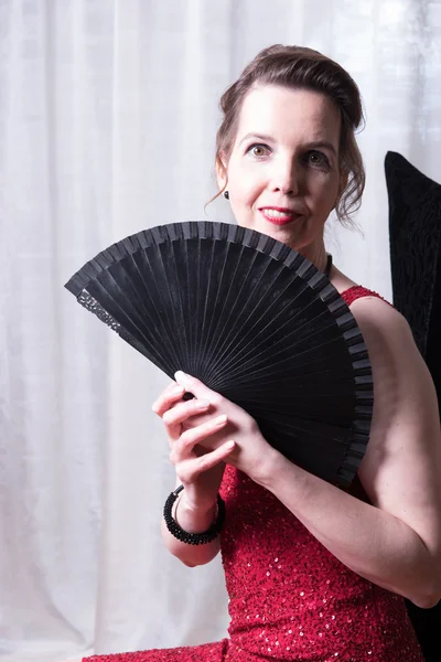 Attractive woman in red dress hiding behind fan — Stock Photo, Image