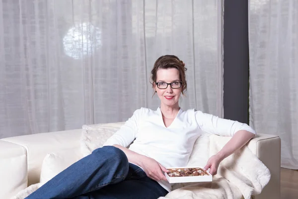 Atrakcyjna kobieta na kanapie jedzenie czekolady — Zdjęcie stockowe
