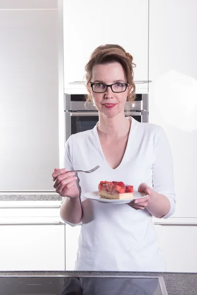 Atractiva mujer en moderno ktchen comer pastel de fresa — Foto de Stock