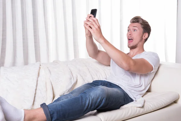 Portrait young man sitting on couch and eating chips and zapping — Stock Photo, Image