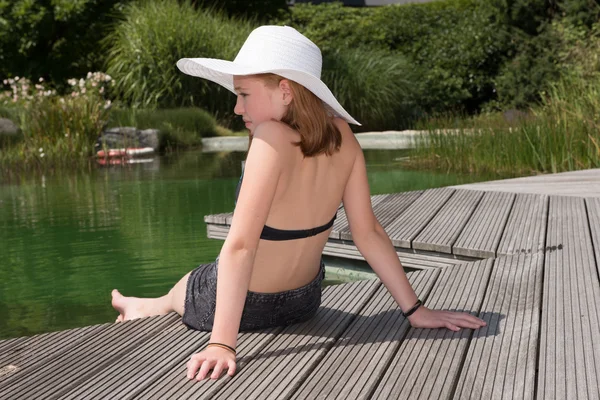 Littel chica con sombrero sentado en la piscina y mirando en el wa — Foto de Stock