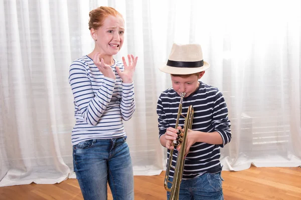 Pojke med hatt spelar trumpet - syster irriterad — Stockfoto