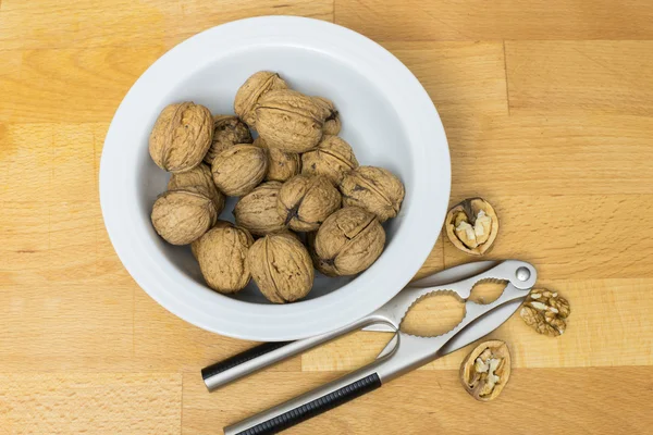 Walnoten in een witte kom en Notenkraker op een houten achtergrond — Stockfoto