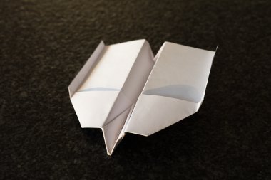 siyah bir zemin üzerine katlanmış beyaz kağıt uçak