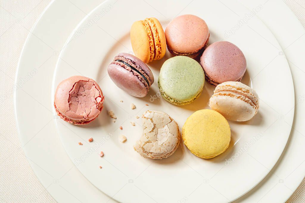 Multicolored delicious french macaroons or macarons lying in a light plate on a white table, top view