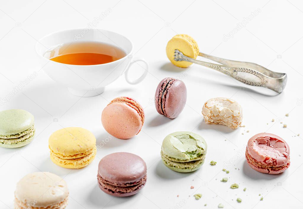 Multicolored delicious French macaroons or macarons lying in a mess and a cup of tea on a white table