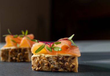 Krem peynirli küçük tahıllı sandviçler, füme somon ve arka planda pancar filizleri.