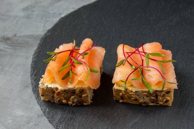 Mikroyeşillikli sağlıklı sandviçler - füme somonlu mısır ekmeği tostları, krem peynir ve gri arka planda pancar lahanası