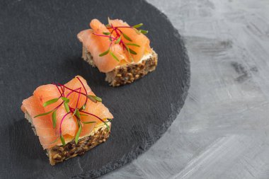 Mikroyeşillikli sağlıklı atıştırmalıklar - krem peynirli mısır ekmekli sandviçler, füme somon ve gri arka planda pancar lahanası.