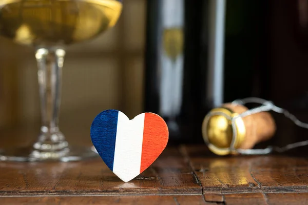 A heart in the colors of the French flag, a glass and a french champagne bottle cork in the background, on the dark old table, Bastille Day and French National Day concept