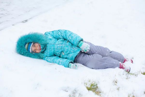 Happy kid girl child outdoors in winter lying on snow — Stock Photo, Image