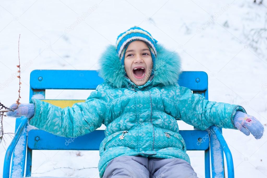 Happy kid girl child outdoors in winter sitting on bench