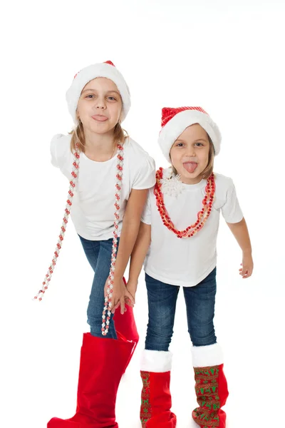 Happy sisters in santa's hats showing off tongues teasing — Stock Photo, Image