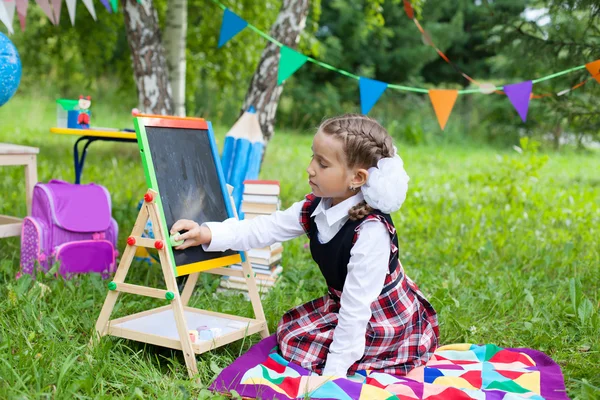 Niño colegiala feliz niña sentada en la hierba y escribiendo en —  Fotos de Stock