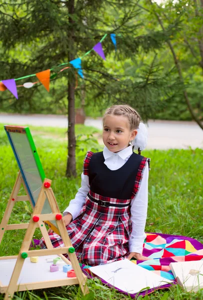 Happy schoolgirl child kid girl sitting on grass and writing on — Stock Photo, Image