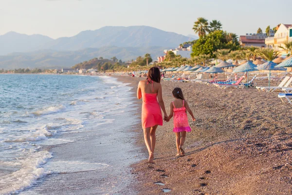 Mamma och hennes lilla dotter gå längs stranden på sunset — Stockfoto