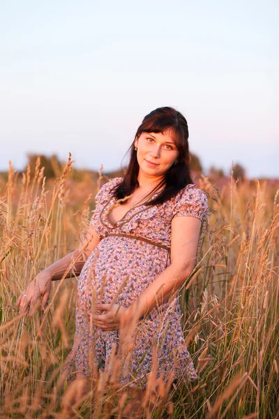 Hermosa joven embarazada feliz chica en el campo, sonriendo y — Foto de Stock