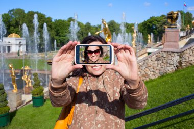 Happy girl tourist shooting selfie in Peterhof in Saint Petersbu