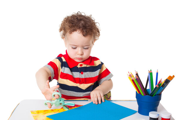 Cute happy baby boy cutting colorful paper
