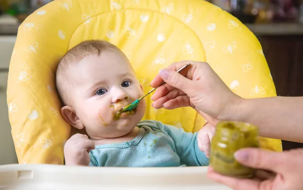 Little baby is eating broccoli vegetable puree. Selective focus. people. — Stock Image Little Baby Eating Broccoli Vegetable Puree Selective Focus People Royalty Free Stock Photos
