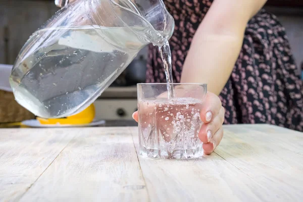 The girl pours water into a glass. Selective focus. Drink.