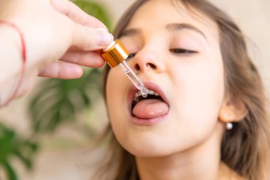 Anne çocuğuna damlatıcıyla vitamin damlası veriyor. Çocuklar için beslenme takviyeleri. Seçici odak.