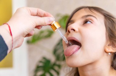Anne çocuğuna damlatıcıyla vitamin damlası veriyor. Çocuklar için beslenme takviyeleri. Seçici odak.