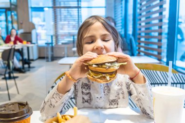 Küçük kız büyük bir burger yiyor. Seçici odak.