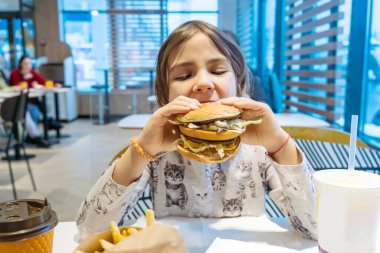 Küçük kız büyük bir burger yiyor. Seçici odak.