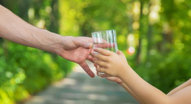 Baba çocuğa bir bardak taze su verir. Seçici odaklanma. Doğa.