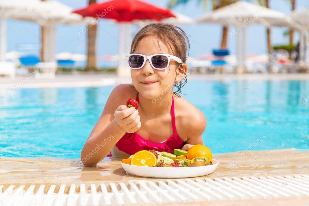 The child eats fruit near the pool. Selective focus. Kid.