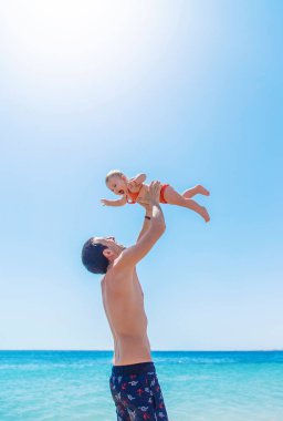 Baba bebeği denizin arka planına fırlatır. Seçici odaklanma. Çocuk.