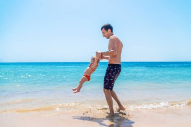 Baba bebeği denizin arka planına fırlatır. Seçici odaklanma. Çocuk.