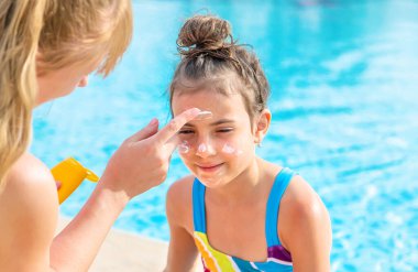Çocuk anneye güneş kremi sürüyor. Seçici odaklanma. Doğa.