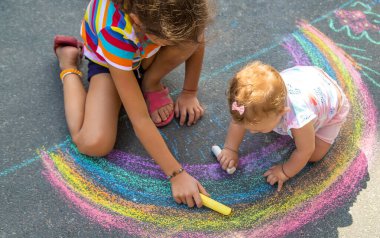 Çocuk asfalta tebeşirle bir ev ve gökkuşağı çizer. Seçici odaklanma. Çocuklar.