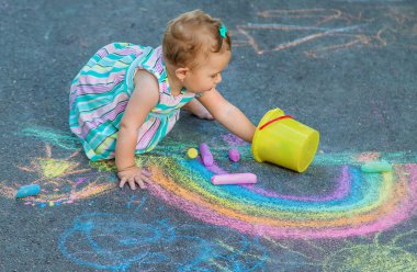 Bebek kaldırıma tebeşirle gökkuşağı çiziyor. Seçici odaklanma. Doğa.