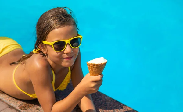 The child is eating ice cream near the pool. Selective focus. Kid.