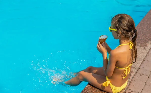 The child is eating ice cream near the pool. Selective focus. Kid.