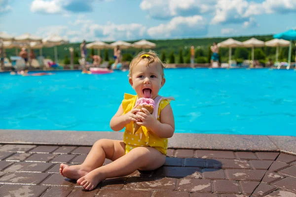 The child is eating ice cream near the pool. Selective focus. Kid.