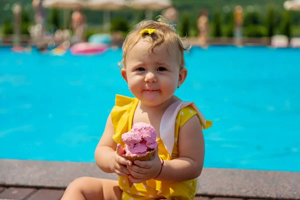 The child is eating ice cream near the pool. Selective focus. Kid.